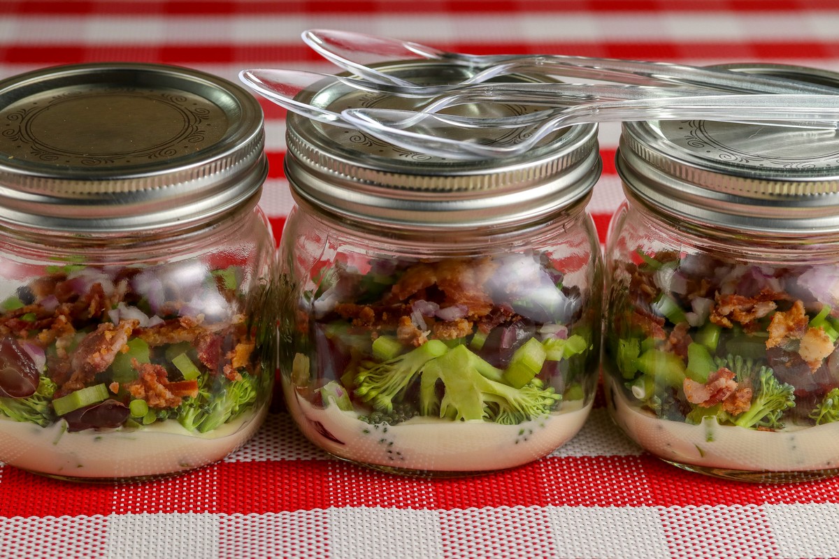 Broccoli Bacon Salad in three glass mason jars with lids on red & white chequered table cloth